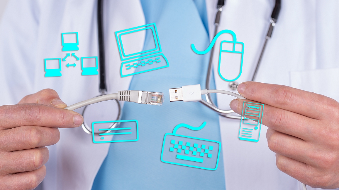 Hände einer Person in weißem Kittel und mit Stethoskop um den Hals halten Netzwerk- und USB-Kabel