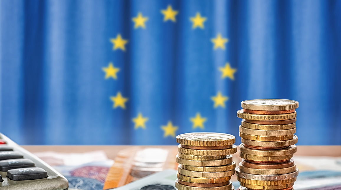 Euros in Scheinen und Münzen vor einer EU-Flagge